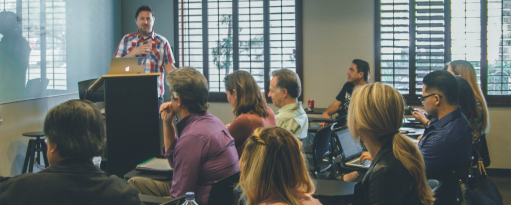 Klassrum där en instruktör talar till en sittande publik.